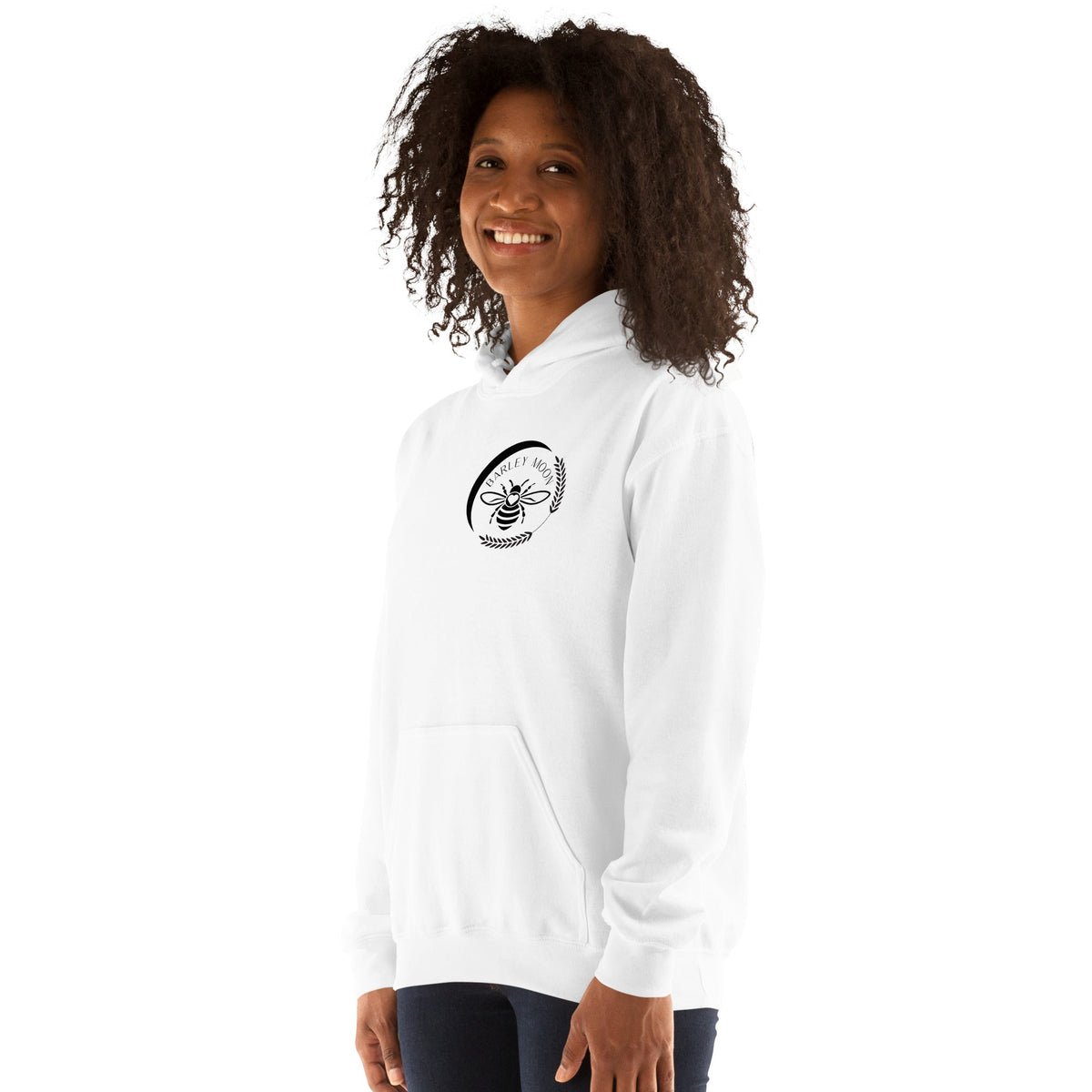 A woman wearing a white Barley Moon Botanicals unisex hoodie with a black bee and crescent moon logo on the chest.