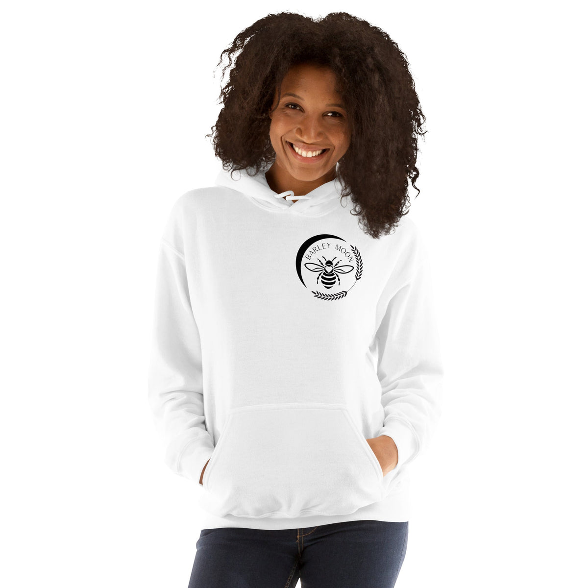 A woman wearing a white Barley Moon Botanicals unisex hoodie with a black bee and crescent moon logo on the chest.