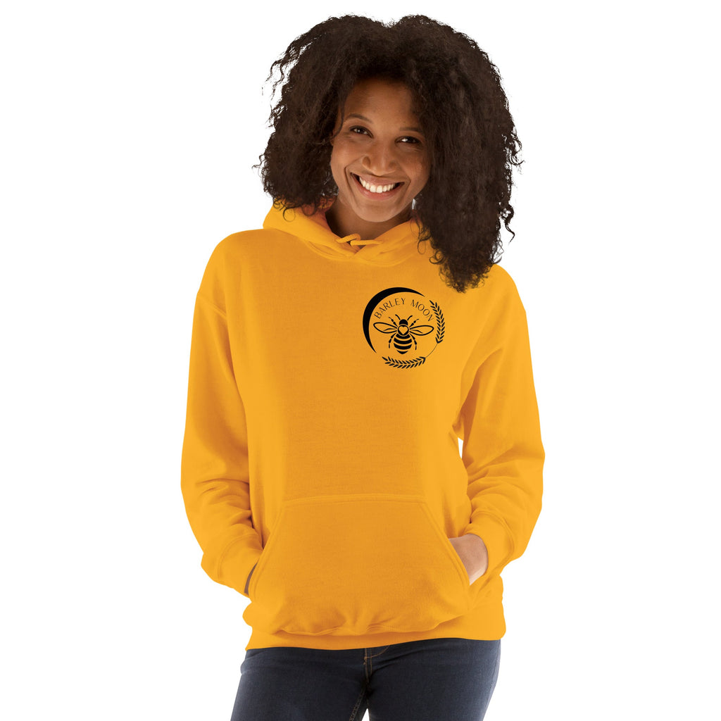 A smiling woman wearing a bright yellow Barley Moon Botanicals unisex hoodie with a black bee and moon logo.