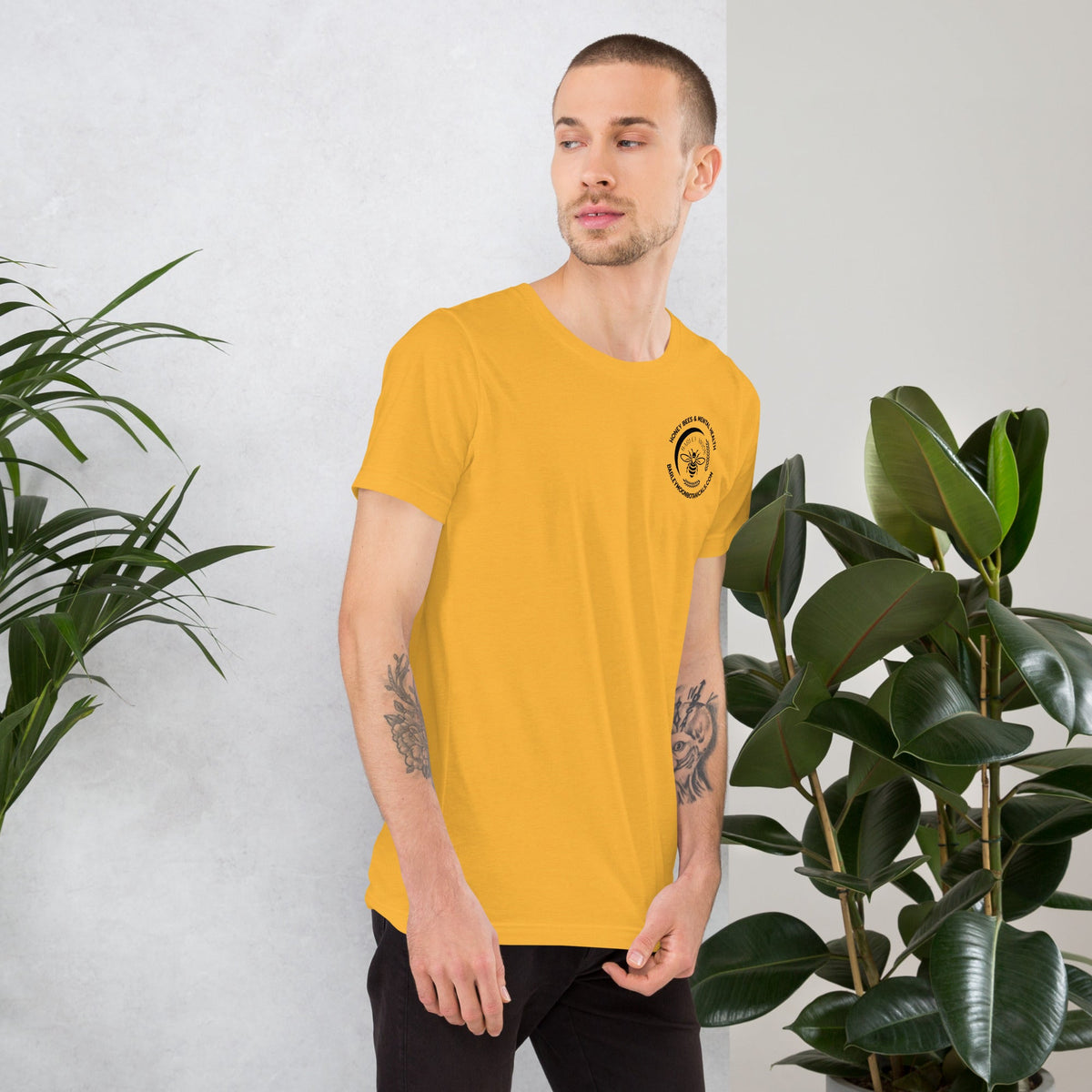 Barley Moon Botanicals unisex yellow cotton t-shirt with a small bee logo on the chest worn by a man near plants.
